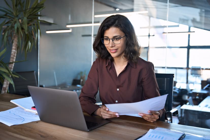 Young business woman working on laptop computer reading financial document report in office.