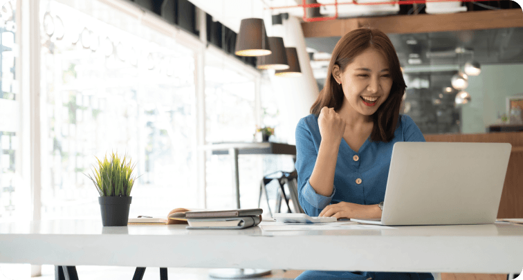 Image of a young Asian businesswomen show joyful expression of success at work smiling happily with a laptop computer in a modern office.