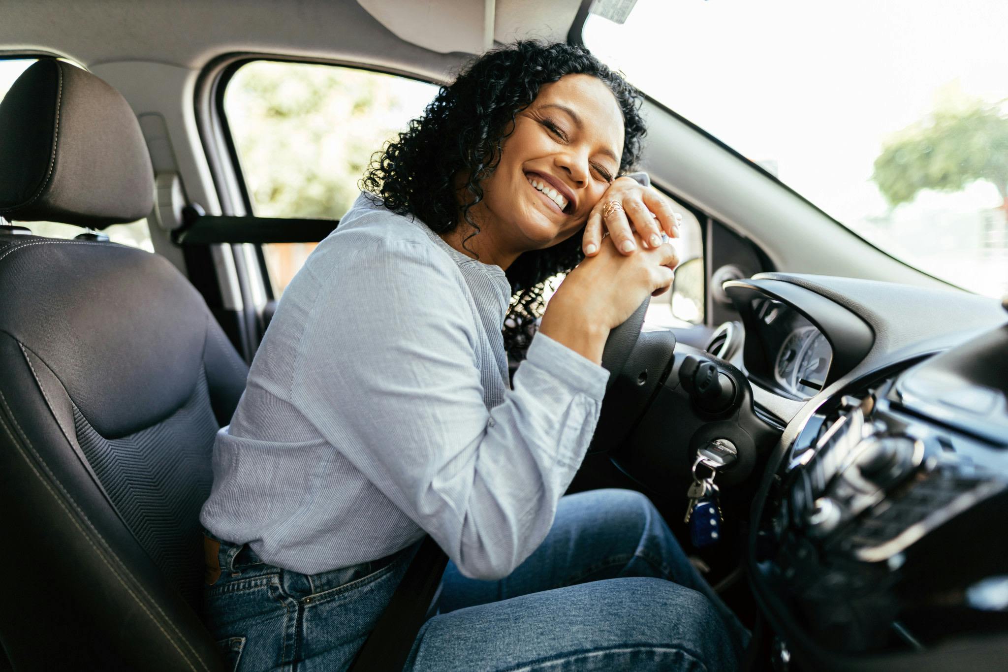 Woman sitting in car lying against the wheel happily.